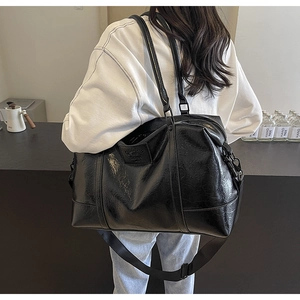 Detail of glossy black leather travel bag with embossed logo and wide shoulder strap