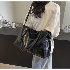 Detail of black glossy faux leather tote bag with sturdy handles and nylon shoulder strap