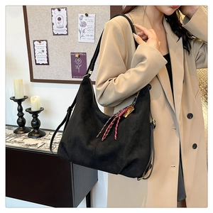 Detail of black suede hobo bag with woven rope charm and adjustable leather strap