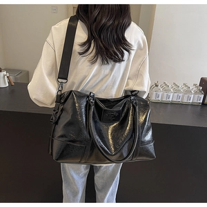 Glossy black large travel tote bag with adjustable shoulder strap shown on a model