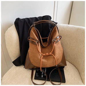 Close-up of brown suede bucket bag with leather handles and drawstring on a beige sofa