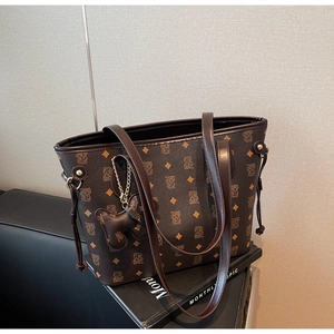 Détail du sac cabas marron foncé montrant le motif monogramme ours et pompon décoratif
