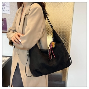 Detail of black matte shoulder bag with woven fringe tassel and metal key pendant decor