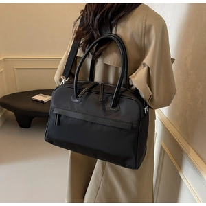 Detail einer großen schwarzen Nylon-Reisetasche, als Schultertasche zum Trenchcoat getragen