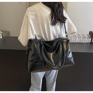 Detail of black glossy PU leather travel bag showing texture and adjustable strap