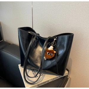 Detail einer glänzenden schwarzen Tote Bag mit braunem Plüsch-Anhänger auf weißem Buch