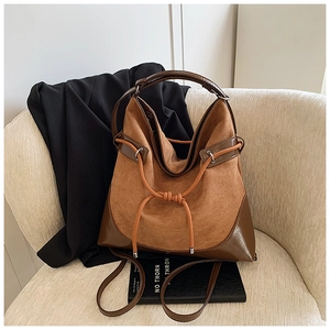 Detail of suede bucket bag with drawstring knot and smooth leather base on a chair