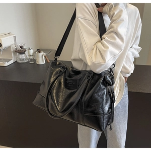 Macro view of large black wax leather travel tote bag showing glossy texture and strap