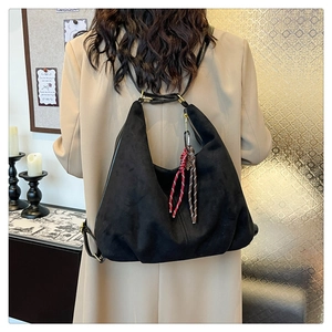 Detail of black suede tote bag with woven tassel and sleek minimalist shoulder strap