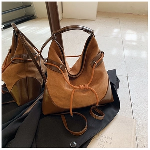 Detail view of large brown suede bucket bag featuring contrast leather trim and drawstring
