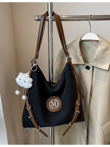 Sac fourre-tout noir avec lanières en cuir marron et logo M porté sur un trench beige