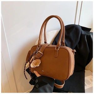 Dettaglio della borsa Boston in pelle caramello con ciondolo da baseball e manici superiori