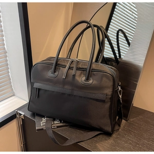 Detailansicht der großen schwarzen Reisetasche aus Nylon mit Ledergriffen auf dem Schrank