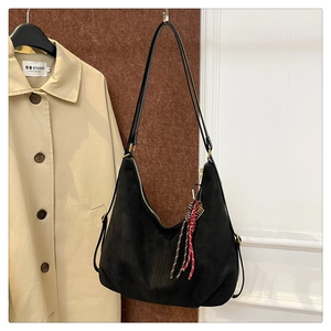Detail view of black matte hobo bag with braided tassel hanging on a wall hook