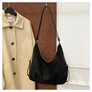 Detail of black suede hobo bag with gold hardware and contrast stitching on a beige coat