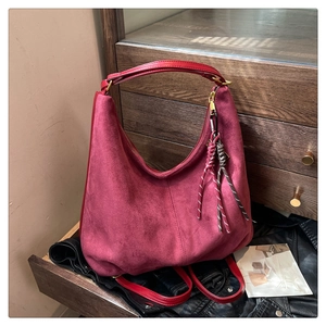 Detail view of burgundy faux suede hobo bag with zip closure and woven tassel