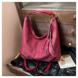Detail of burgundy suede hobo bag with contrast leather straps and woven tassel