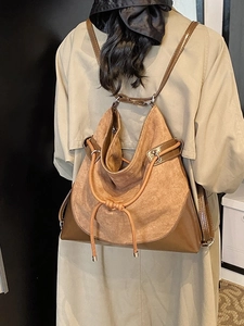 Large tan suede hobo backpack with dark leather trim shown on a model in a minimal room