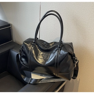 Detail of black glossy crinkled leather travel bag with dual handles on leather seat