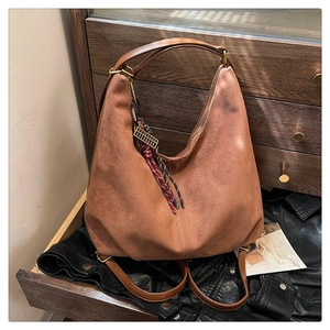 Detail of brown suede Hobo bag with bronze zipper and woven pendant on vintage wood surface