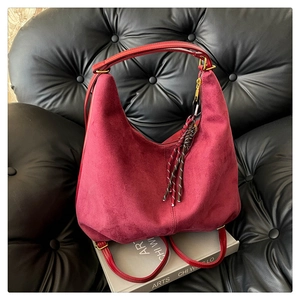 Detail of burgundy faux suede hobo bag with colorful woven rope charm and gold hardware