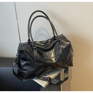 Macro detail of glossy crinkled leather finish and dual handles on a black travel bag