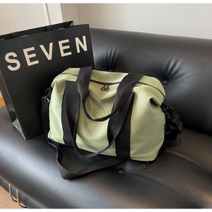 Gros plan du sac de voyage en nylon vert clair avec broderie dorée sur canapé en cuir