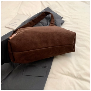Detail of dark brown suede tote bag featuring smooth matte texture and integrated wide strap