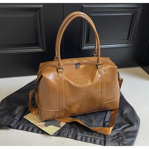 Detail of a brown glossy PU leather travel bag with reinforced stitching and logo plate