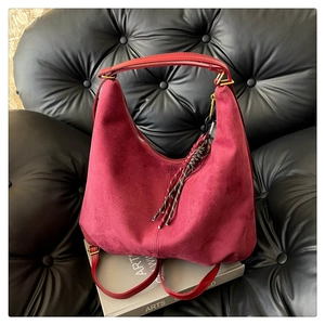 Close-up of burgundy frosted suede hobo bag with red woven pendant on leather sofa