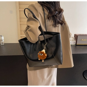 Nahaufnahme einer schwarzen Lackleder-Tote Bag mit einem braunen Plüsch-Sonnenbrillen-Anhänger