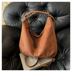Detail of brown suede hobo bag with red tassel on black vintage leather sofa