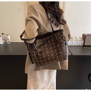 Sac fourre-tout marron foncé à motif monogramme et breloque porté par un mannequin