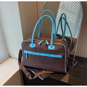 Detail einer großen braunen Reisetasche mit blauen Lederakzenten auf einem Holztisch