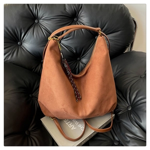 Detailed close-up of brown suede hobo bag texture on leather sofa with art books