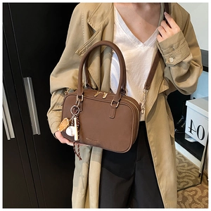 Dettaglio borsa a cuscino in pelle marrone con logo metallico e ciondolo da baseball