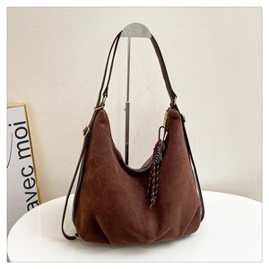 Detail view of coffee suede crescent tote bag with dark leather strap and woven pendant