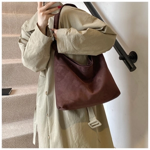 Close-up of a large dark brown suede tote bag carried by a model on stairs