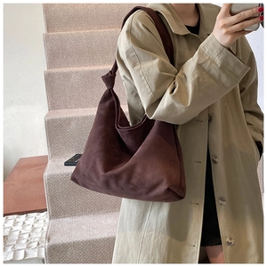 Close-up of brown suede tote bag with knotted shoulder strap on a model in trench coat