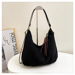 Detail of black suede hobo bag featuring a decorative red and brown braided rope charm