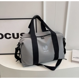 Détail du grand sac de voyage gris avec sangles noires et boucles métalliques dans un décor épuré
