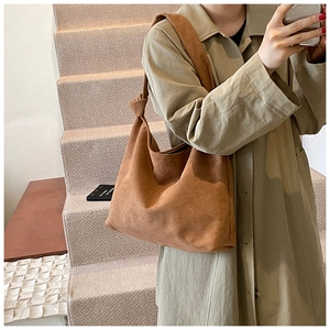 Brown suede tote bag with knot strap detail shown on a model in a minimalist outfit