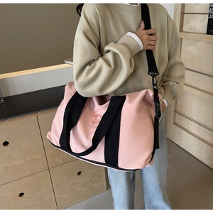 Grand sac de voyage rose en toile avec poignées noires et bandoulière réglable sur une chaise