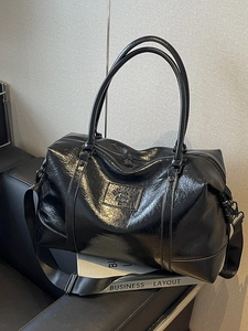 Sleek black glossy travel bag with handles and shoulder strap on a leather sofa