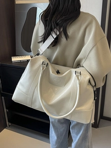 Large cream leather travel bag with adjustable strap worn by a woman for short trips