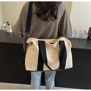 Vue arrière d'un modèle portant un grand sac de voyage en toile beige et noir avec compartiment