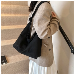 Detail of a minimalist black suede hobo bag featuring a unique knotted shoulder strap