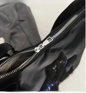Gros plan sur la fermeture éclair en métal argenté et le patch chat en peluche du sac