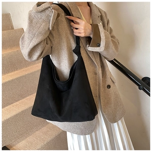 Detail of a black suede tote bag with a unique knot shoulder strap on a female model