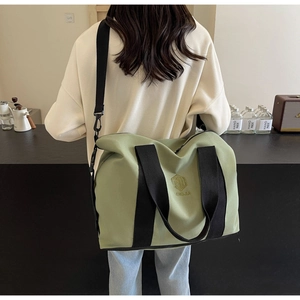 Grand sac de voyage en toile vert olive avec bandoulière porté sur l'épaule de dos